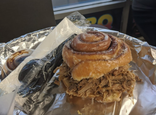 A pulled pork sandwich served on a cinnamon roll, placed on a silver foil wrapper.