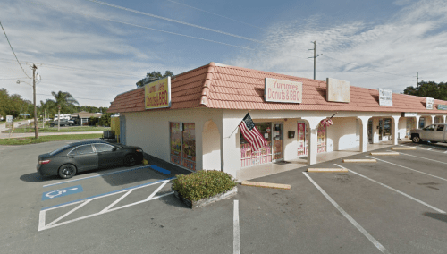 A small storefront with a red-tiled roof, featuring signs for "Yummies Donuts & BBQ" and parked cars outside.