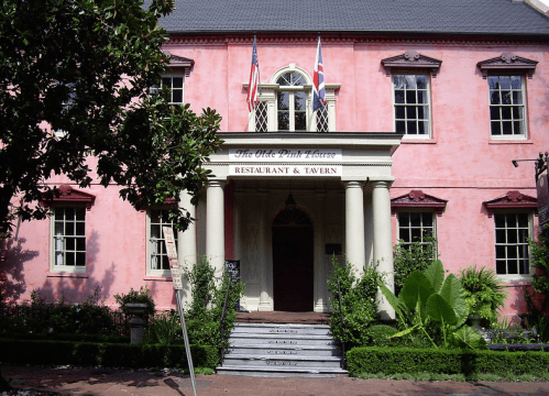 Historic pink building with columns, featuring a sign for "The Old Pink House Restaurant & Tavern" and flags.