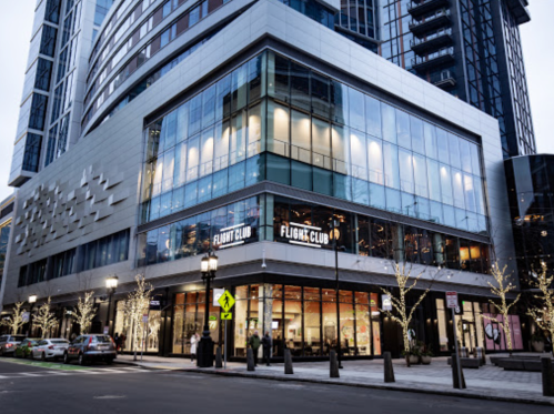Modern building exterior featuring the "Flight Club" storefront, with city lights and trees in the foreground.