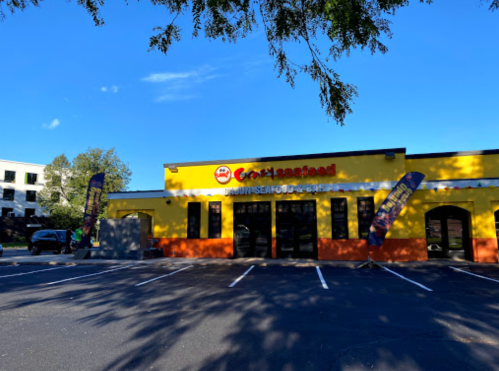 A bright yellow seafood restaurant with banners outside, set against a clear blue sky and nearby trees.