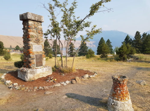 A stone monument surrounded by trees and grass, with a smaller stone structure nearby and mountains in the background.