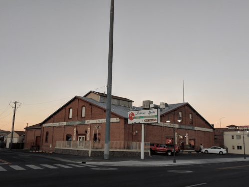 A brick building at sunset, featuring a sign and surrounded by a street and parked cars.