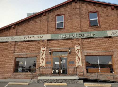 Exterior of a brick building with "Flanigan Square" sign, featuring large windows and a welcoming entrance.