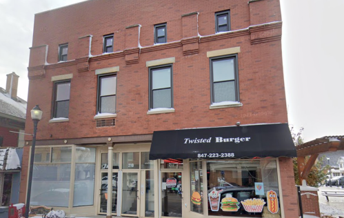 A brick building with a black awning labeled "Twisted Burger" and large windows on the ground floor.