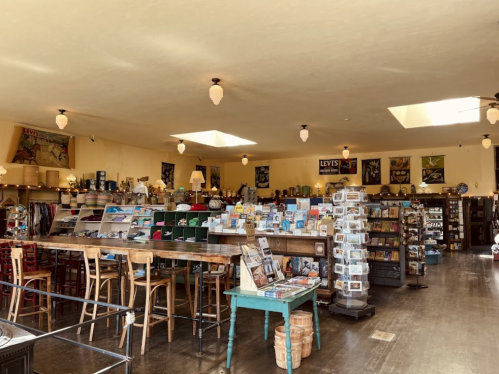 A cozy shop interior with wooden shelves, a counter, and various merchandise, illuminated by pendant lights.