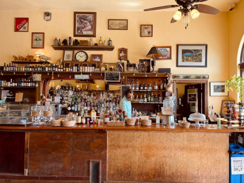 A cozy bar with a wooden counter, shelves of bottles, and a bartender preparing drinks in a warm, inviting atmosphere.