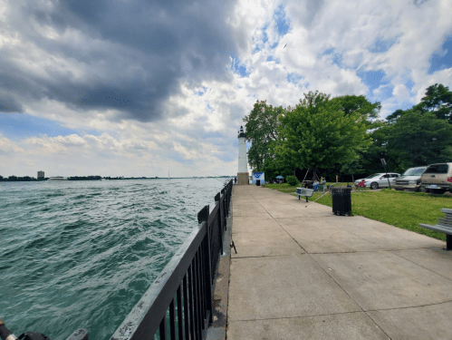 A waterfront scene with a path, trees, and a lighthouse under a cloudy sky, alongside a flowing river.
