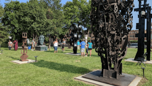 A group of people exploring an outdoor sculpture park filled with various large metal sculptures and greenery.
