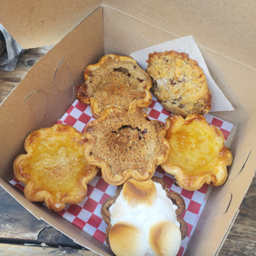 A box containing six assorted baked goods, including pie-like desserts with various fillings and toppings.