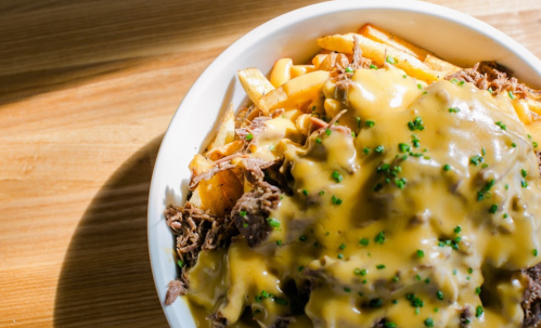 A bowl of loaded fries topped with shredded beef and melted cheese, garnished with green herbs.