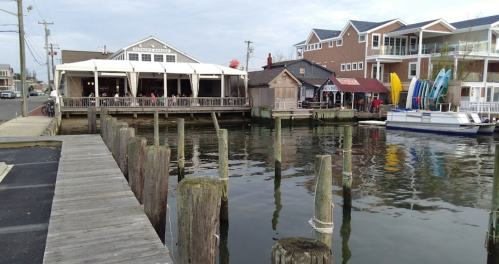 A waterfront scene featuring a restaurant, boats, and wooden posts along a calm waterway with nearby buildings.