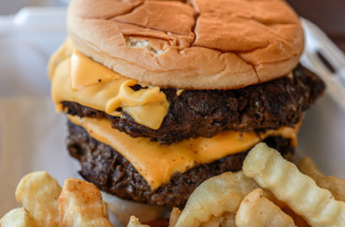 A double cheeseburger with melted cheese on a bun, served with crinkle-cut fries on the side.