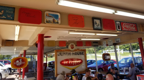 Interior of a diner with vintage signs, red pillars, and patrons seated at tables. Bright and inviting atmosphere.