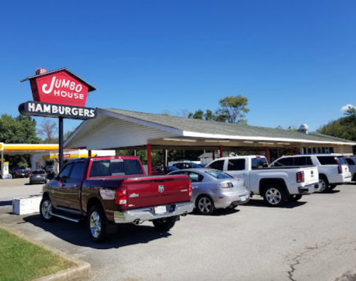 A roadside hamburger restaurant named "Jumbo House" with several parked cars in front under a clear blue sky.