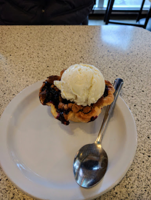 A dessert featuring a cookie bowl filled with dark fruit filling and topped with a scoop of vanilla ice cream.