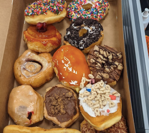 A variety of colorful donuts in a box, featuring sprinkles, chocolate, caramel, and unique toppings.