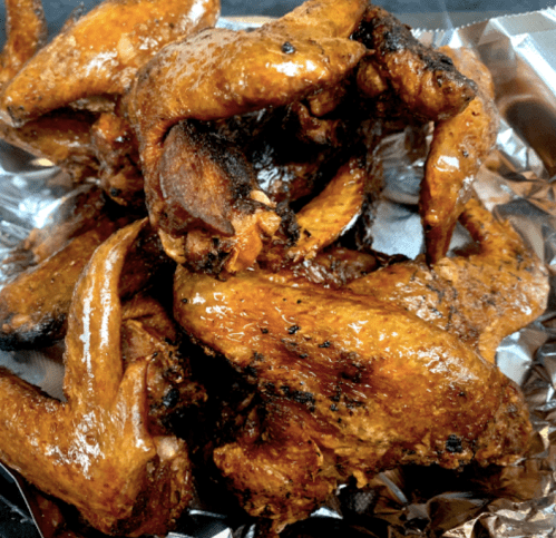 A close-up of glazed, grilled chicken wings piled on aluminum foil.