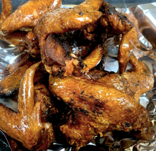 A close-up of glazed, grilled chicken wings piled on aluminum foil.