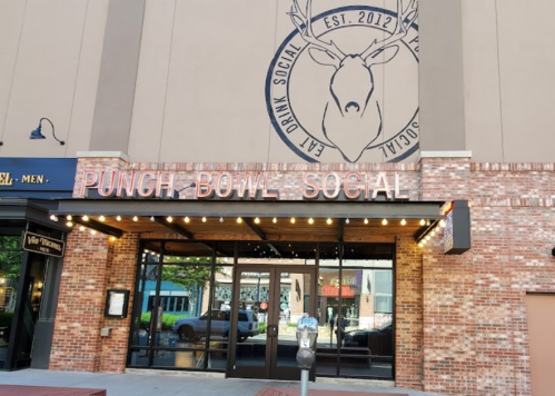 Exterior of Punch Bowl Social, featuring a large deer logo and a brick facade, with large glass doors and marquee lights.