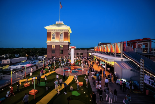 A vibrant outdoor scene at dusk with people enjoying mini-golf and attractions near a historic building.