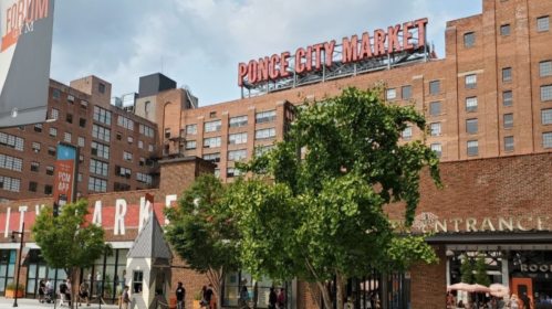 Ponce City Market building with greenery in the foreground and a cloudy sky above.