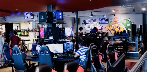A gaming lounge with multiple computers, gaming chairs, and colorful wall art featuring cartoon characters.