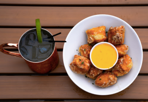 A plate of golden fried snacks with a dipping sauce, alongside a dark cocktail in a copper mug with a lime wedge.
