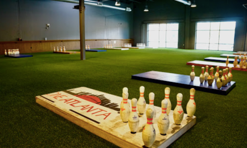 Indoor bowling alley with artificial turf, featuring multiple lanes and bowling pins arranged on wooden platforms.