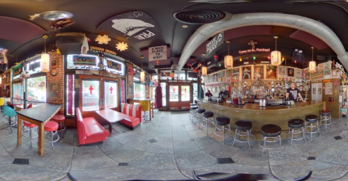 A panoramic view of a vibrant bar with red booths, a long counter, and eclectic decor on the walls.