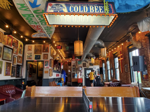 A cozy bar interior with colorful decor, string lights, and a ping pong table, creating a lively atmosphere.