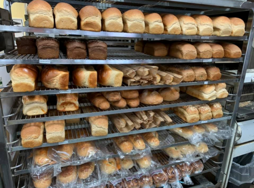 A metal rack filled with various types of bread loaves, including white, brown, and specialty breads, neatly arranged.