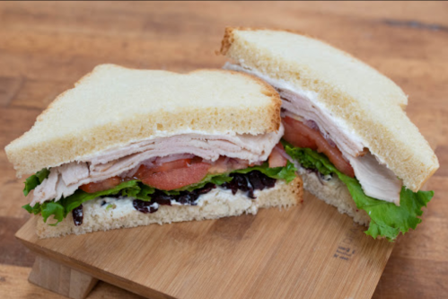 A sandwich with layers of turkey, lettuce, tomato, and a spread, served on white bread, cut in half.