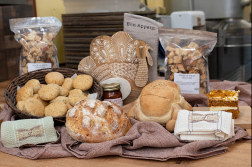 A variety of baked goods including bread, cookies, and a turkey-shaped serving dish, arranged on a table with a cloth.