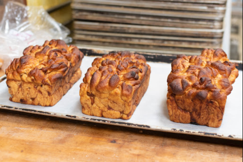 Three freshly baked loaves of bread on a baking tray, with a golden-brown crust and a textured surface.