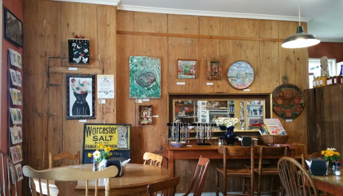 Cozy café interior with wooden walls, art on display, and a round mirror above a wooden counter.