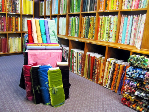 A colorful display of fabric rolls in a craft store, with shelves filled with various patterned and solid fabrics.