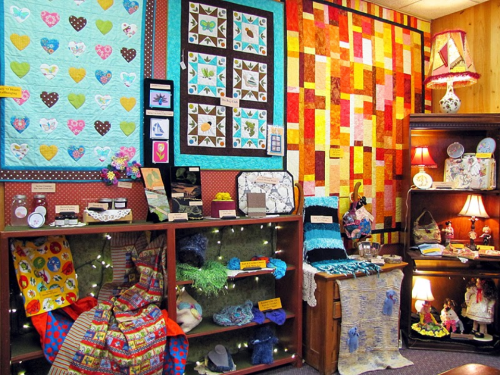 A cozy display of colorful quilts and handmade crafts in a warmly lit room, featuring various textiles and decorative items.