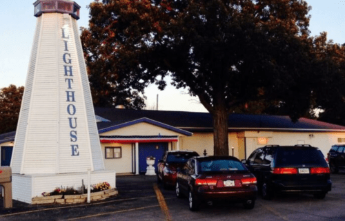 A white lighthouse structure with "Lighthouse" written on it, next to a building and parked cars.