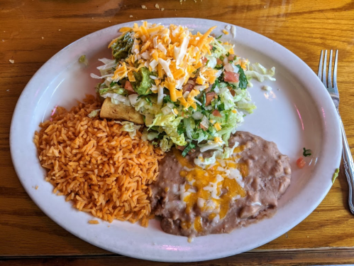 A plate of Mexican food featuring rice, refried beans, a taco topped with lettuce, tomatoes, and cheese.