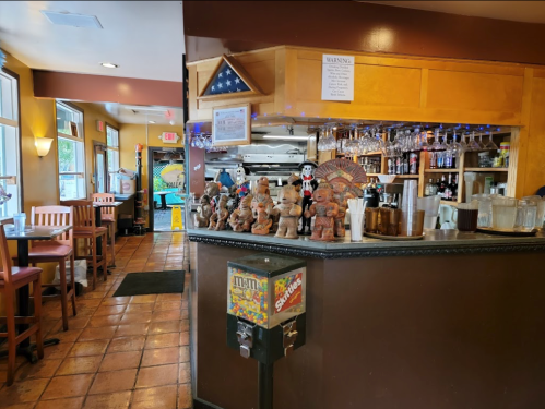 A cozy restaurant interior featuring a bar with decorative figures, seating, and a colorful gumball machine.