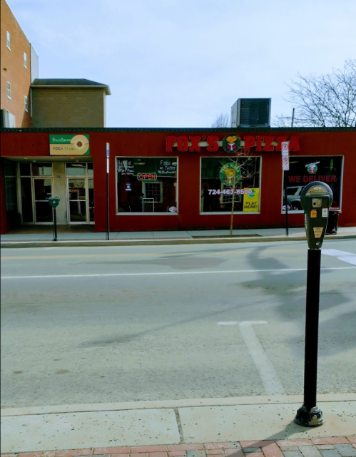 A red pizza shop named "Fox's Pizza" with a delivery sign, located on a street with a parking meter in front.