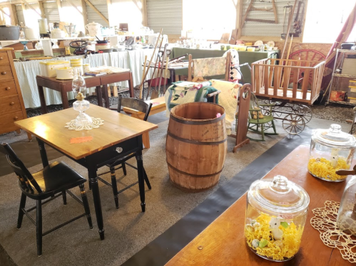 A cozy vintage shop interior featuring furniture, decor, and collectibles, including a table, barrel, and glass jars.