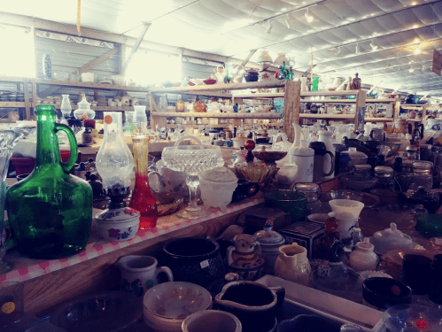 A bustling antique shop filled with various glassware, ceramics, and collectibles on wooden shelves.
