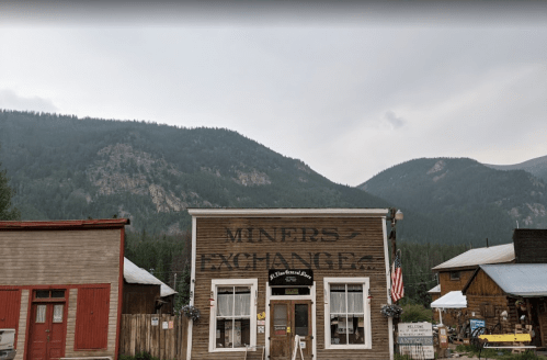 Historic building labeled "Miners Exchange" with mountains in the background and an American flag hanging outside.
