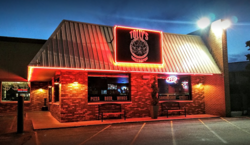 A brightly lit restaurant exterior with a sign reading "Tolly's," featuring neon lights and a welcoming atmosphere.