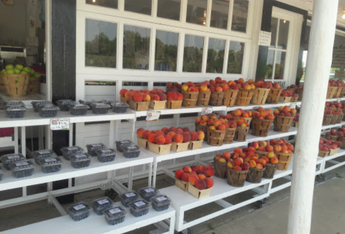 A fruit stand displaying baskets of peaches and containers of blueberries outside a shop.