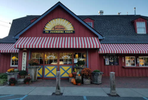 Red barn-style building with a welcoming sign, striped awning, and autumn decorations outside.
