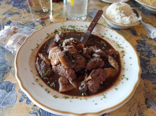 A plate of beef stew with mushrooms, garnished with parsley, served with a side of rice.