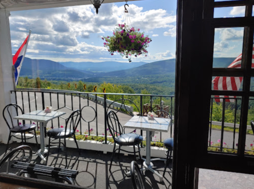 A scenic view from a café with tables and chairs overlooking mountains and a blue sky with clouds.
